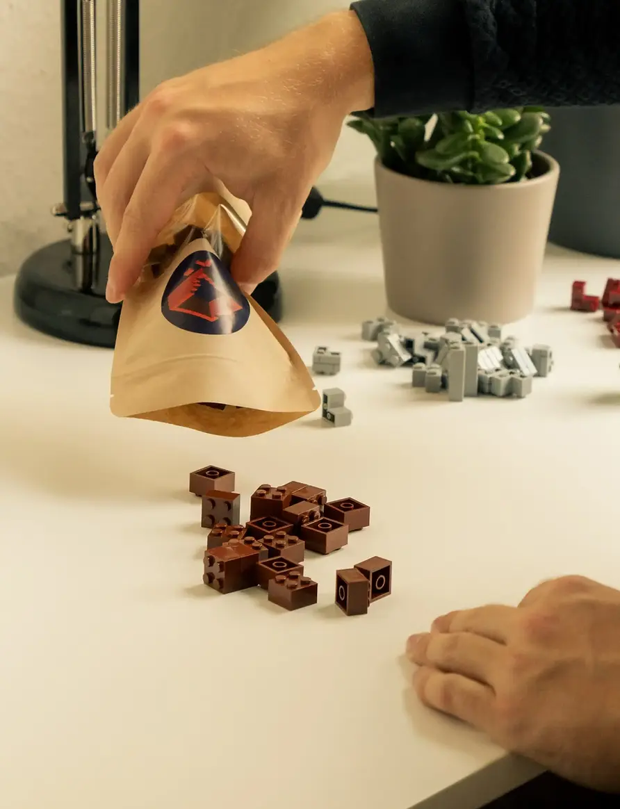 Ein Penny Bricks Beutel, aus dem viele 2x2 Klemmbausteine auf einen Bautisch fallen